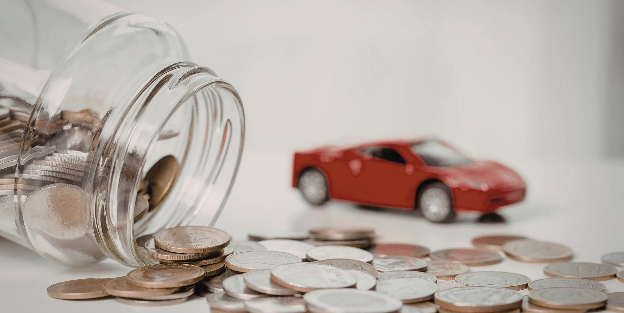 Bocal de pièces renversé devant une petite voiture de collection rouge