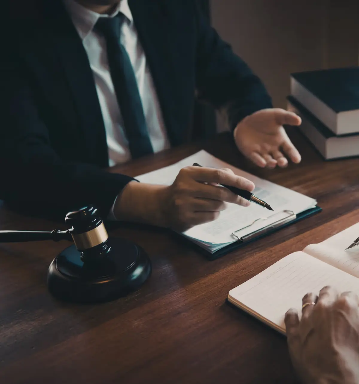 Avocat en costume avec maillet de juge, carnet et piles de livres de droit sur un bureau
