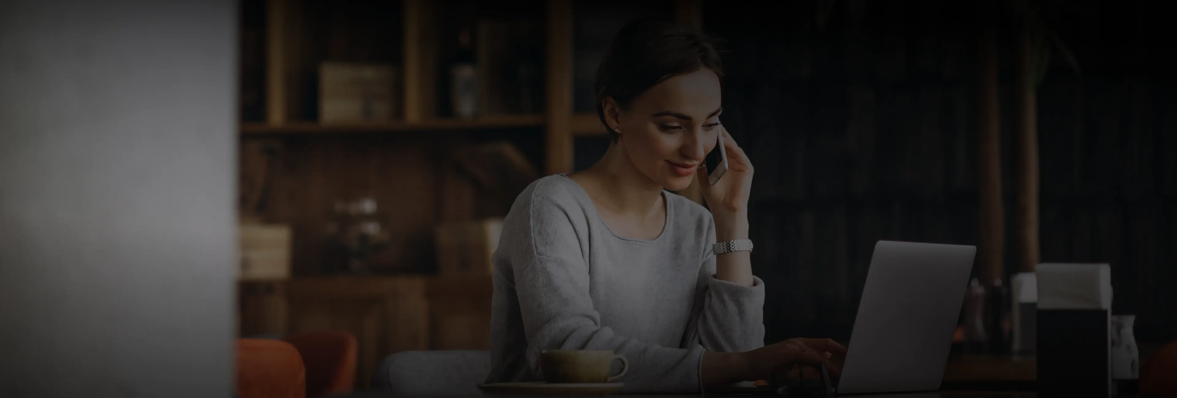 Une femme au téléphone, souriante, consulte son ordinateur portable dans un café